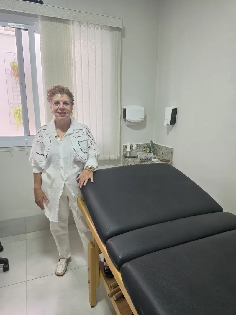 Beth Perez ao lado da maca de tratamento no consultório